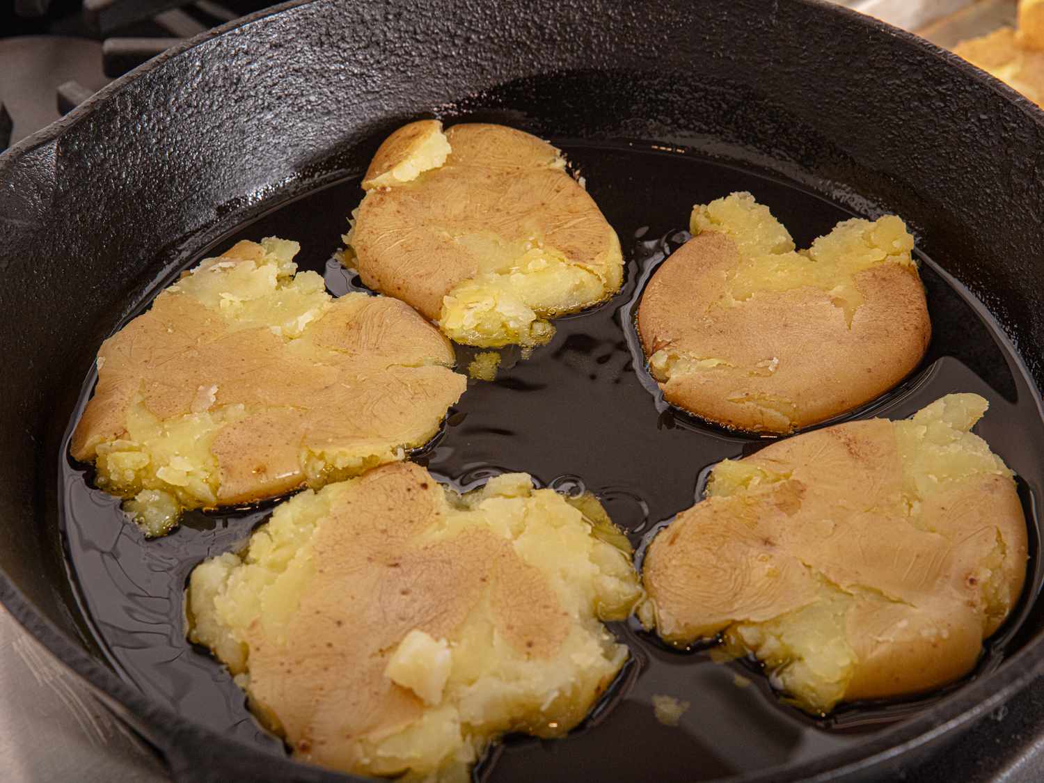Smashed potatoes cooking in a skillet with oil