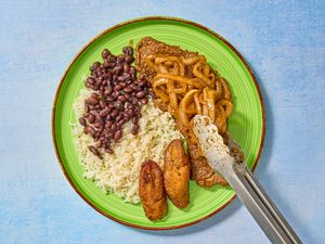 Onions placed on top of steaks, with sides of rice, plantains and beans 