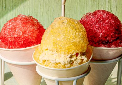 Three snow cones in paper cups one yellow in the center and red ones on the sides