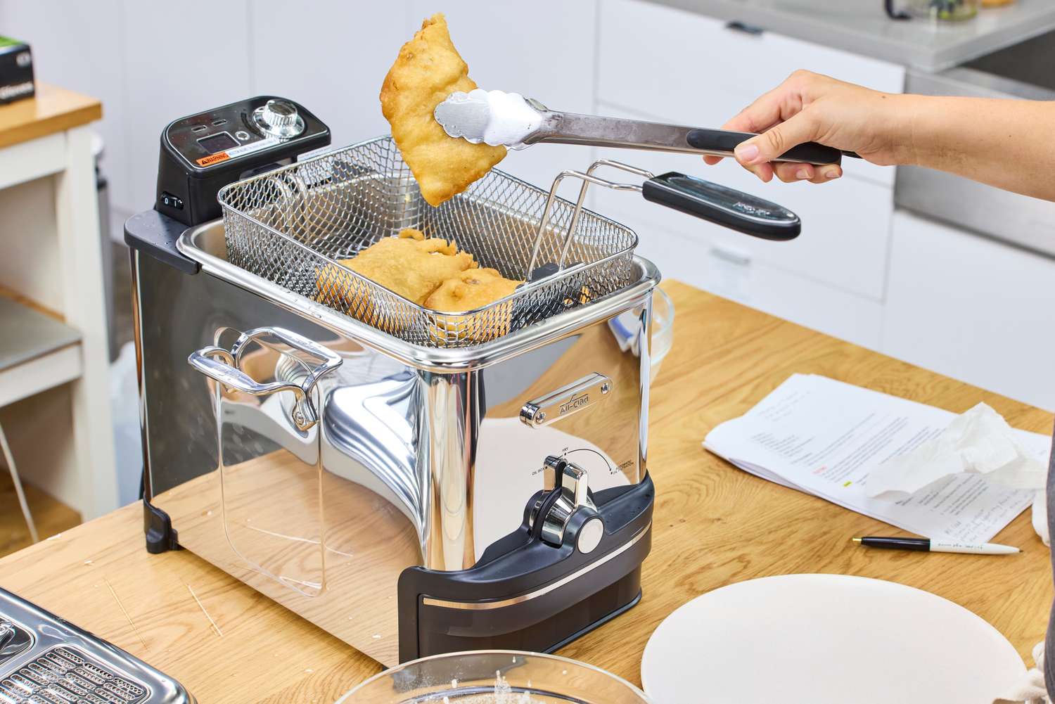 A person lifts fried food from the All-Clad Easy Clean Pro 3.5L Electric Deep Fryer with tongs