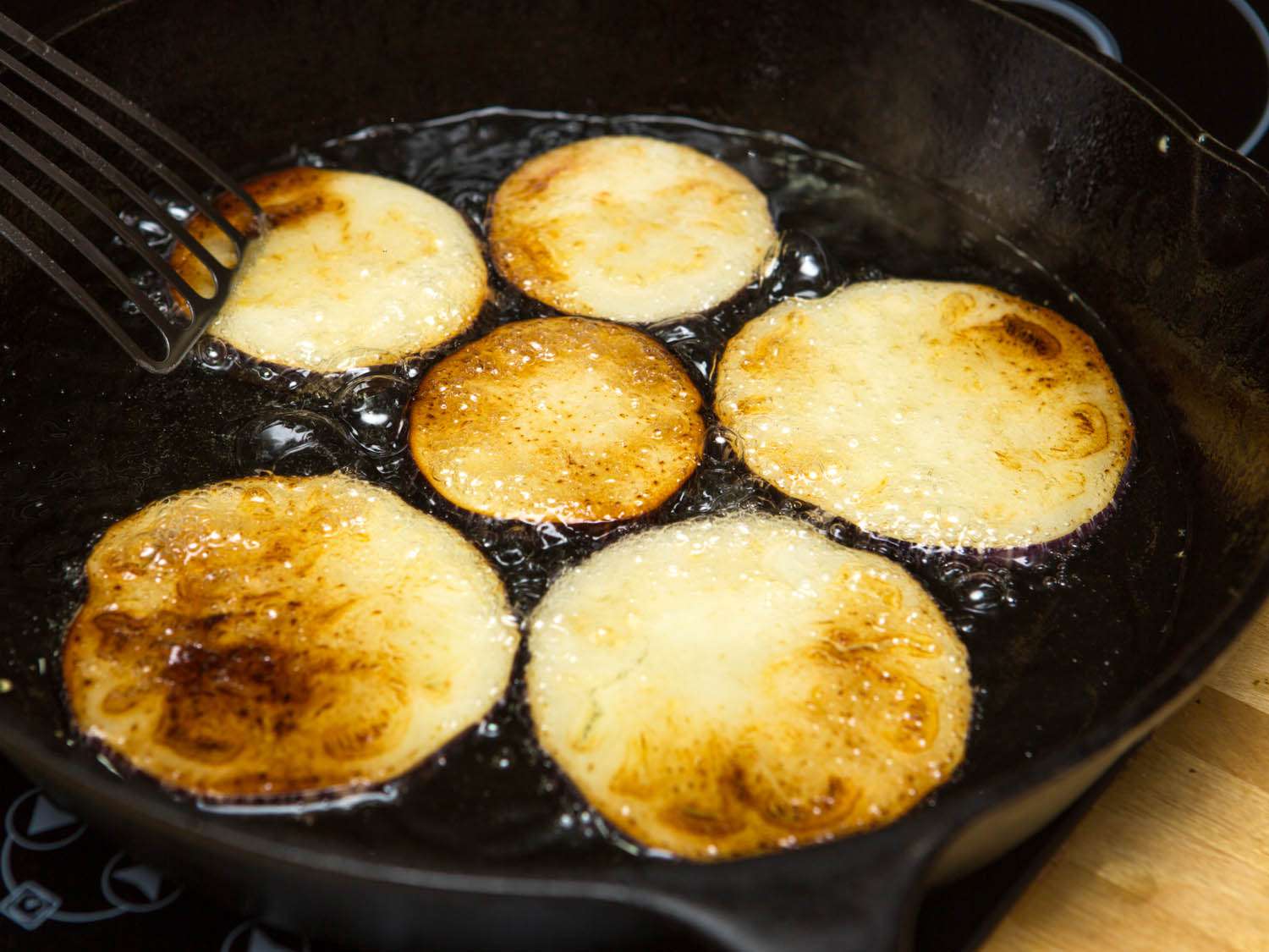 Eggplant slices are being fried in a cast iron skillet. 