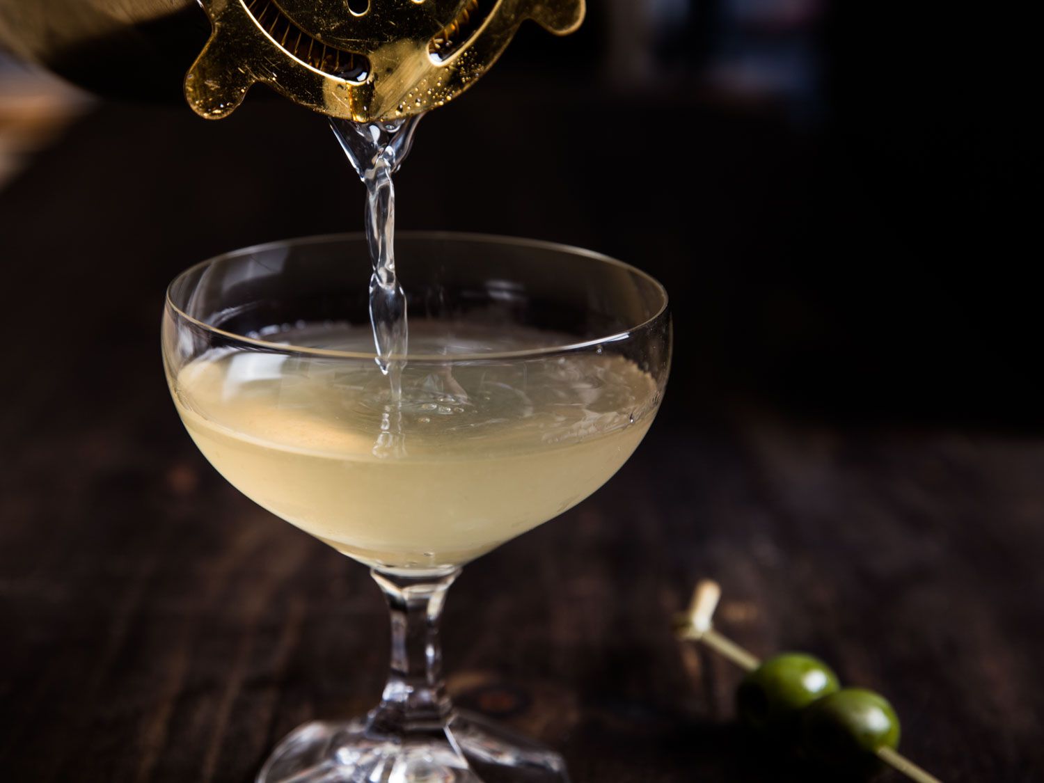 Straining a dirty mezcal martini into a coupe cocktail glass.