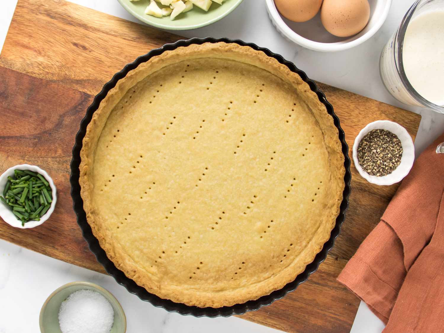 pate brisee on a wooden board, with bowls of eggs and butter to the side. 