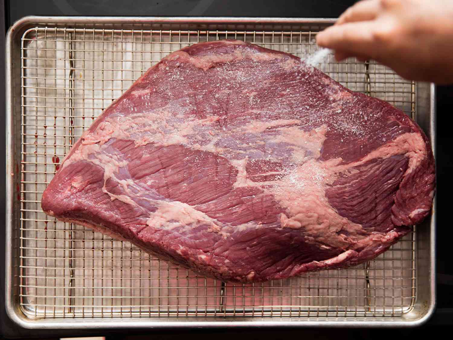 Overhead shot of the flat, or first cut, of brisket, sitting on a wire rack in a rimmed baking sheet.