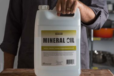 Hand holding a large jug of mineral oil on a wooden counter