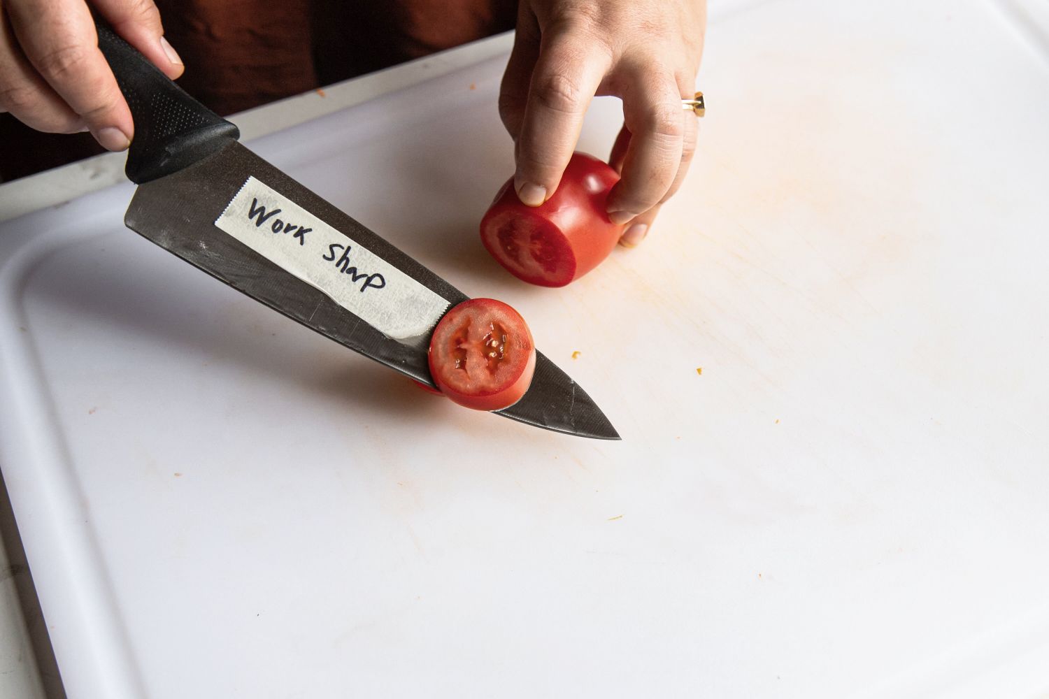 A person using a knife to slice a tomato