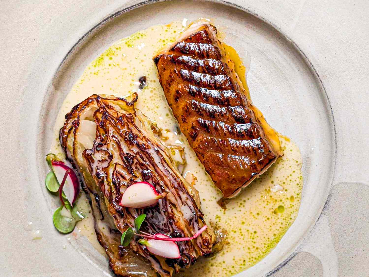A plate featuring a seared fish fillet and charred cabbage with garnish
