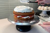 Layer cake being frosted with icing placed on a rotating cake stand