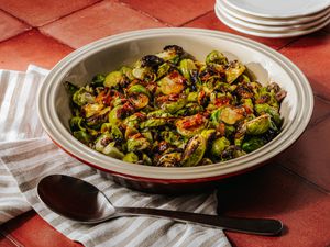Bowl of roasted brussel sprouts on a brick surface, with a striped towl and spoon 