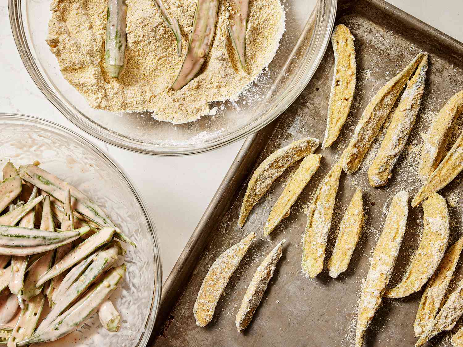 2 bowls, one with okra in buttermilk mixture, one with okra dredged in cornmeal mixture, and then a sheetpan with prepared okra 