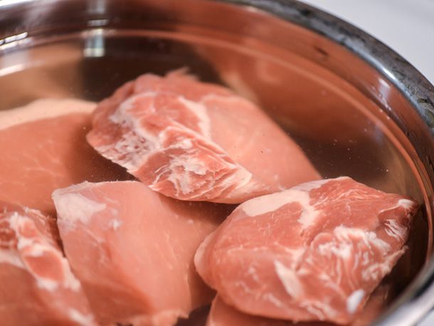 Boneless pork chops are submerged in a brine.