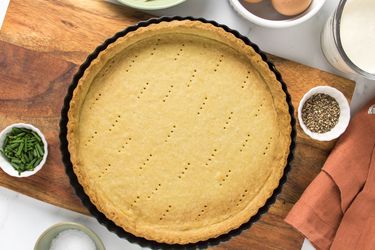 pate brisee on a wooden board, with bowls of eggs and butter to the side. 