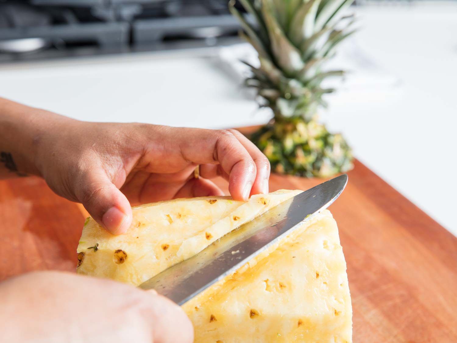 A knife cutting diagonally along the eyes of a pineapple.