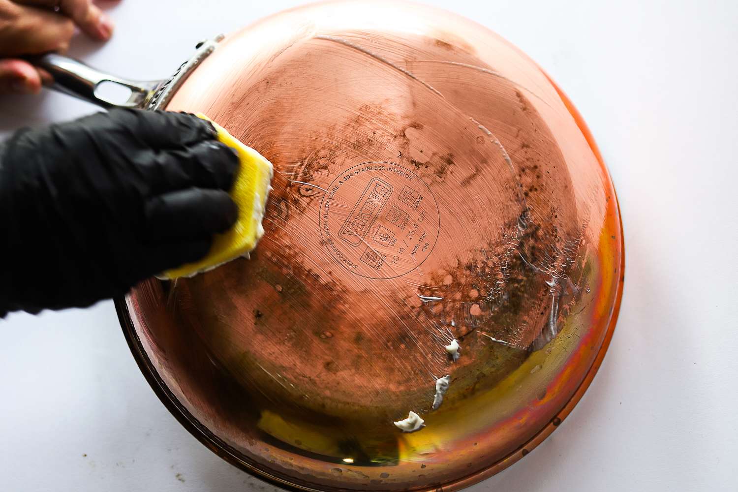 Closeup of someone cleaning the bottom of a metal pan with a sponge and gloves