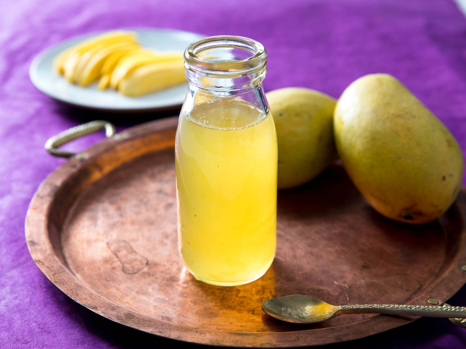 Open bottle of homemade mango syrup with fresh mangoes on the background. 