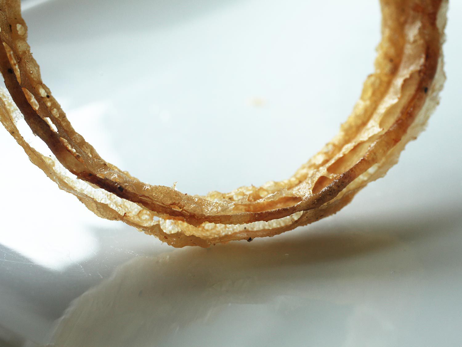 An onion ring is held up to reveal a split between layers of the onion flesh.
