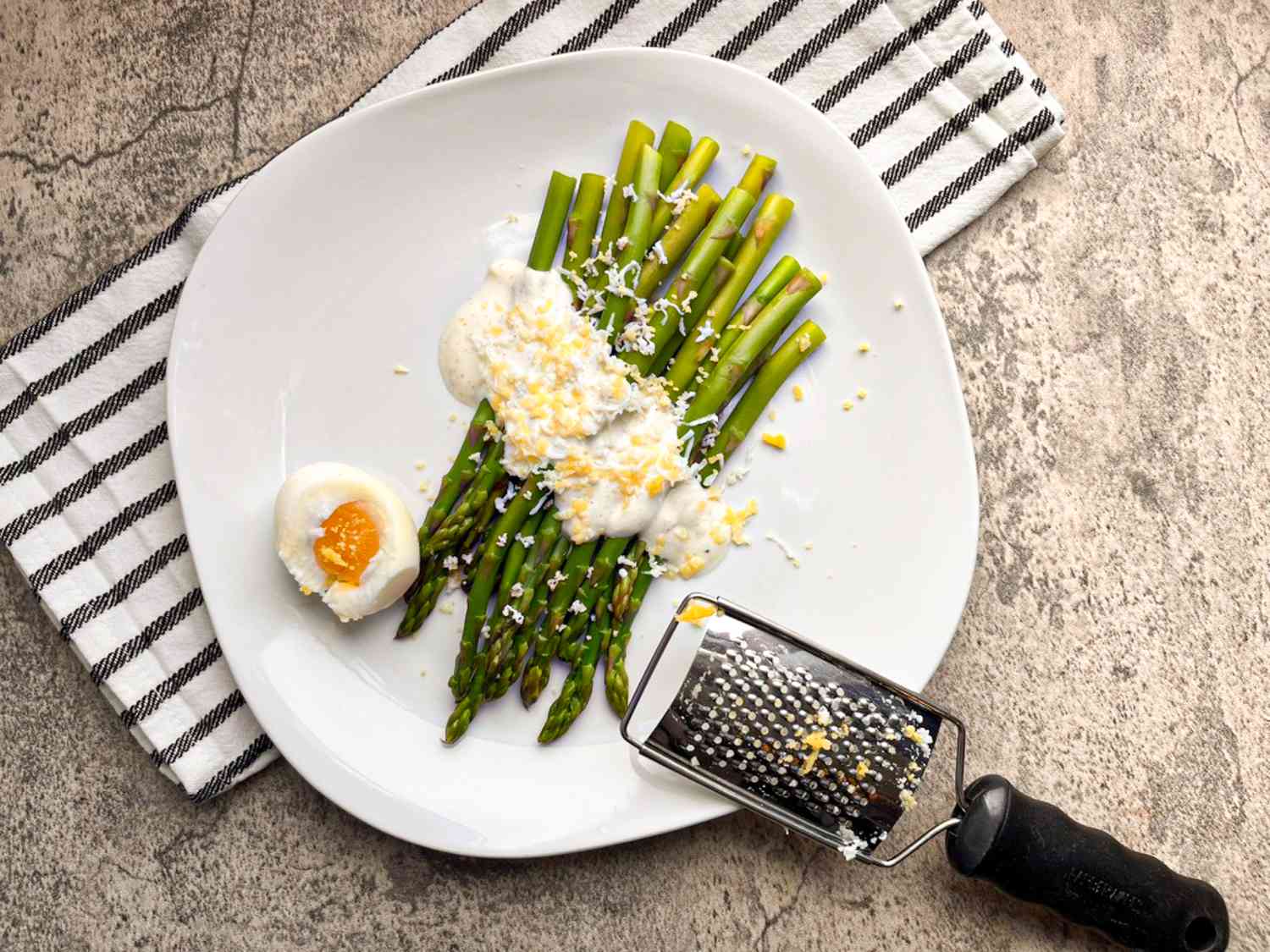 A plate of asparagus with yogurt sauce and egg grated on top