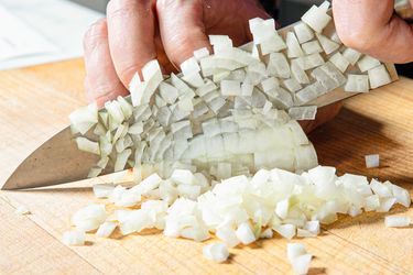 A person finely dicing an onion with a knife on a wooden cutting board