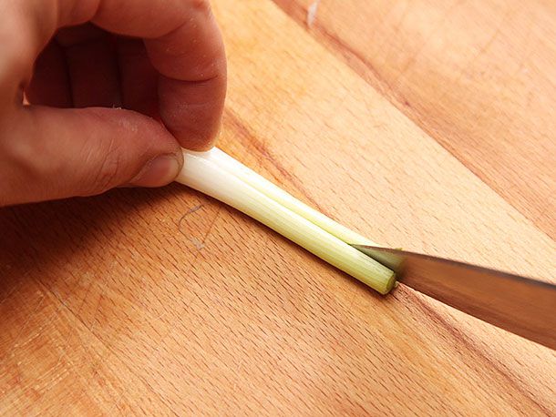 A scallion being cut in half length-wise.