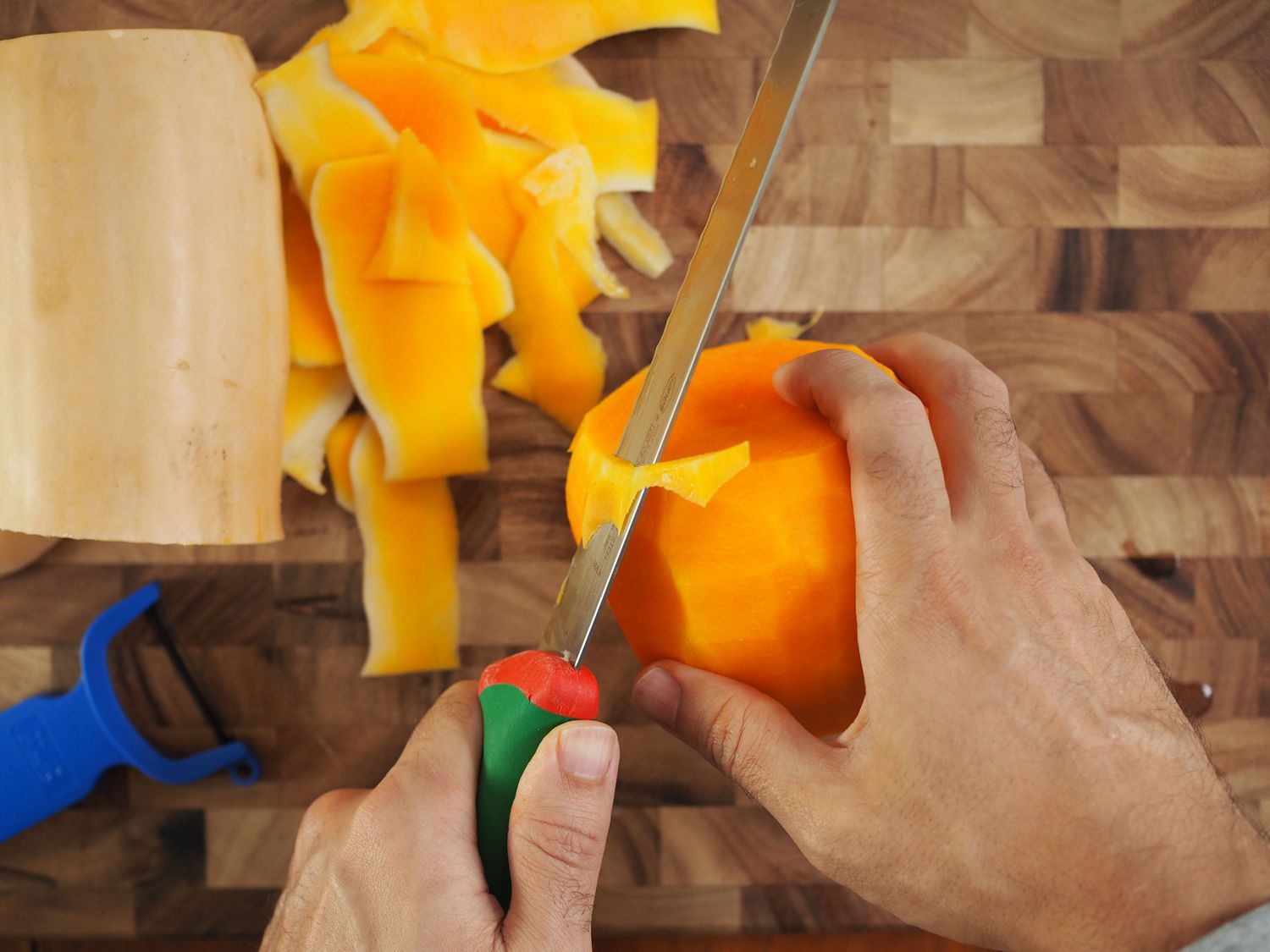 A slicing knife trimming the edges of a peeled butternut squash.