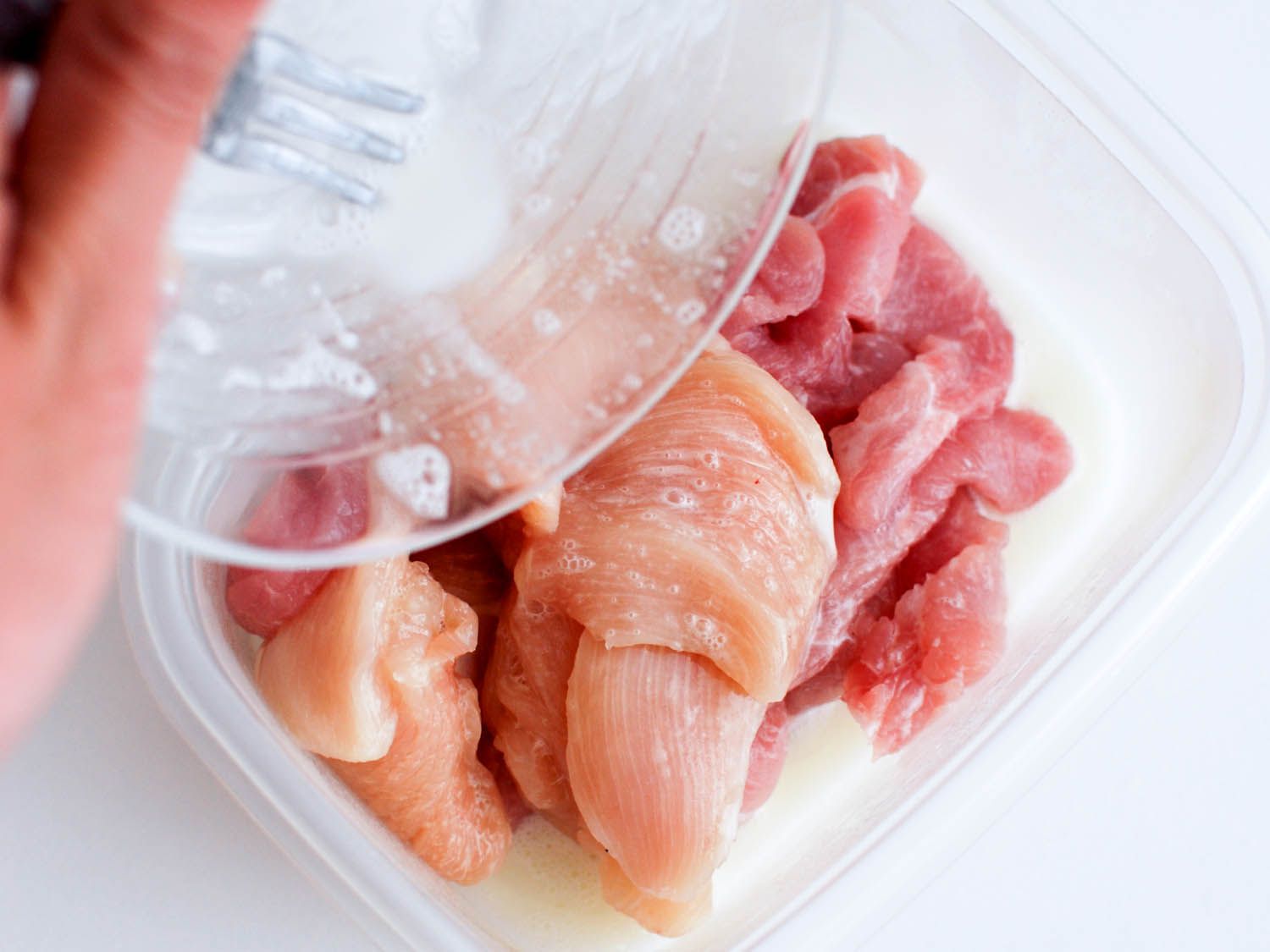 Velveting marinade being poured over pieces of chicken and pork.