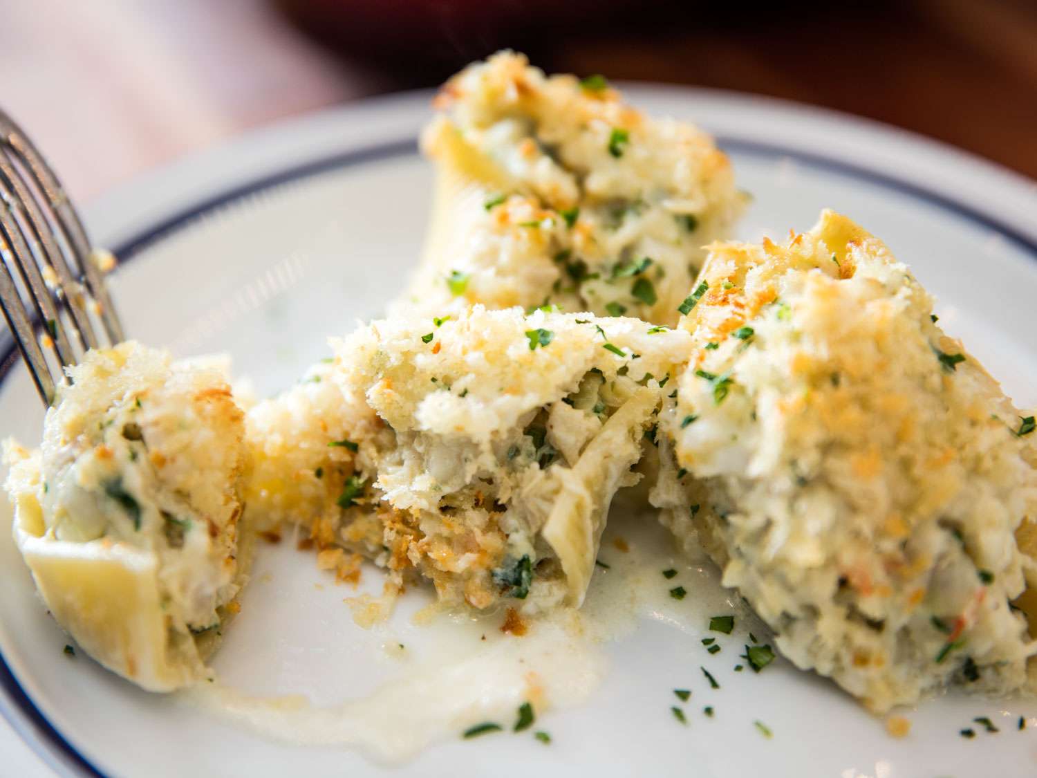 A fork splitting seafood stuffed pasta shell.