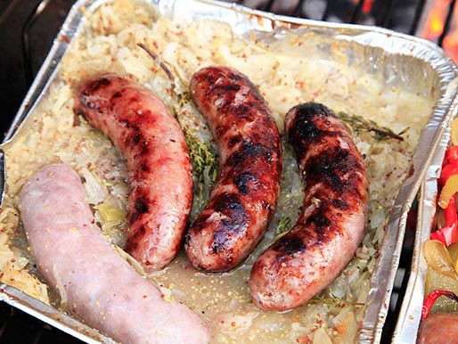 An aluminum pan with sauerkraut and mustard, with three cooked sausages and one uncooked sausage