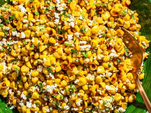Esquites Mexican street corn salad with cheese and garnish, served in a green dish with a spoon