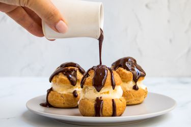 A trio of profiteroles being doused in chocolate sauce