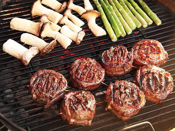 Stuffed and grilled flank steaks sitting on barbecue near grilled mushrooms and asparagus