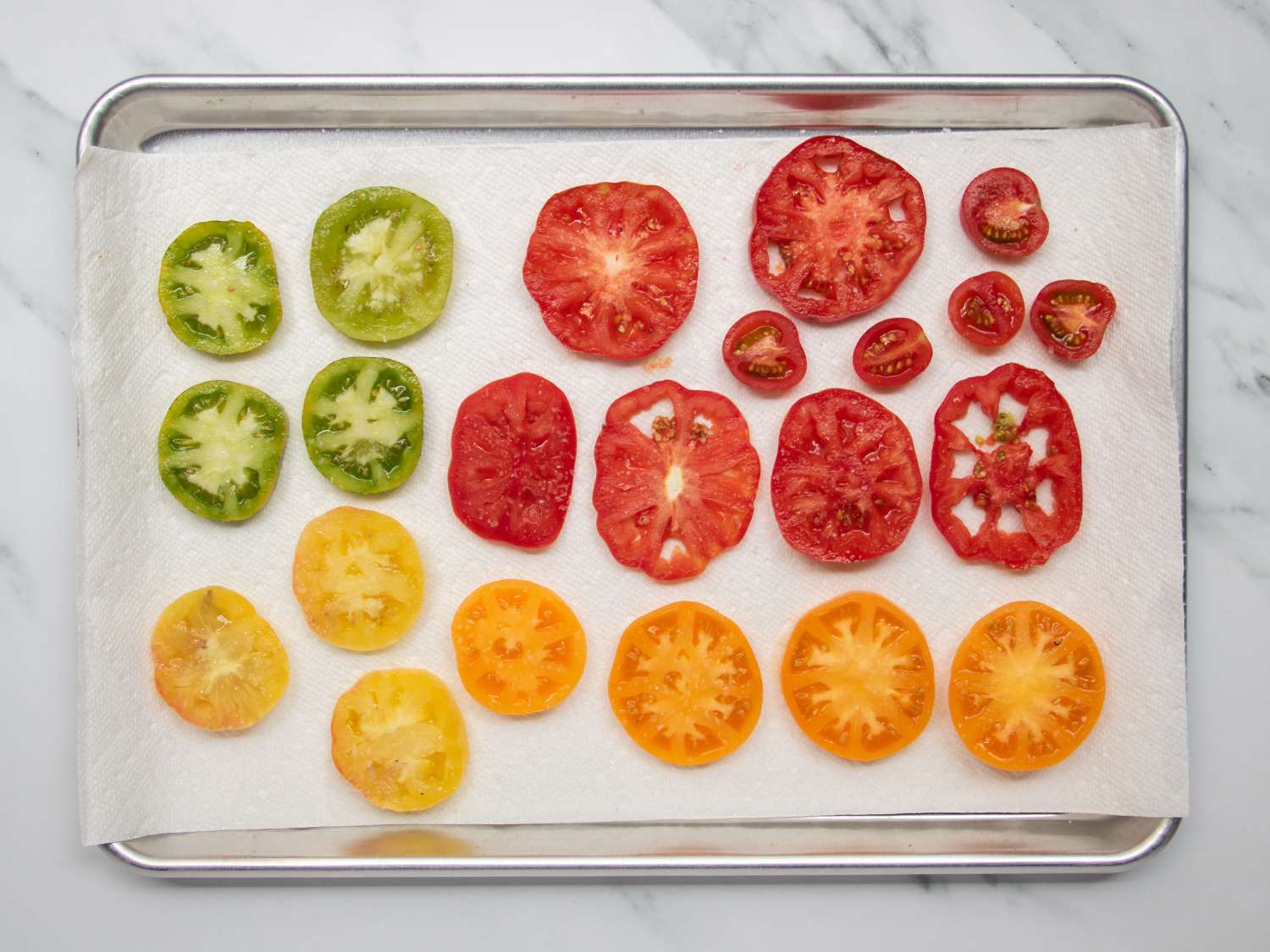 Sliced tomatoes in variety placed on a paper towel-lined rimmed baking sheet