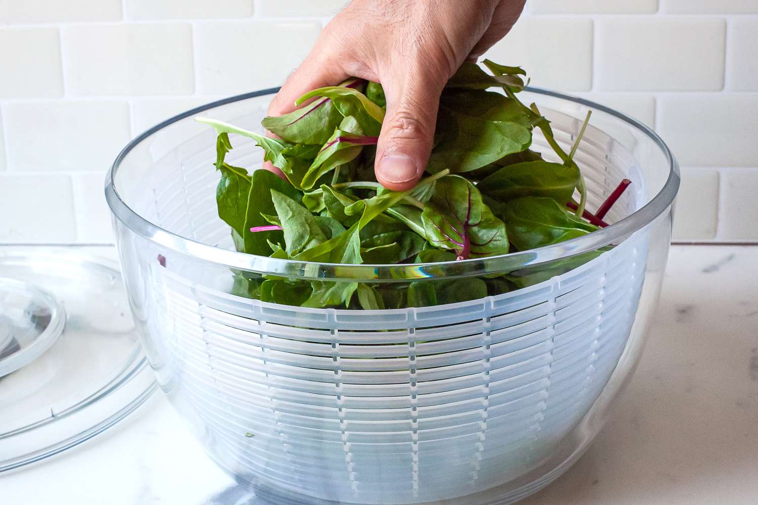 a person placing mixed greens into a salad spinner
