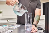 A hand pouring water into the water compartment of the Ninja Thirsti Drink System