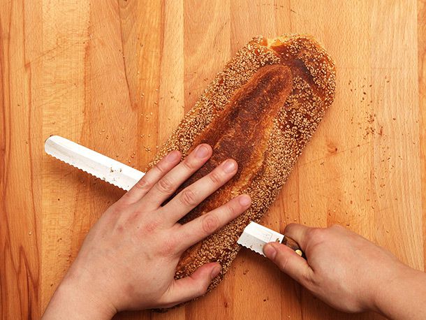 overhead view of slicing crusty loaf in half horizontally with a serrated bread knife