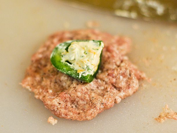 A flattened ball of uncooked sausage with a stuffed jalapeño piece.