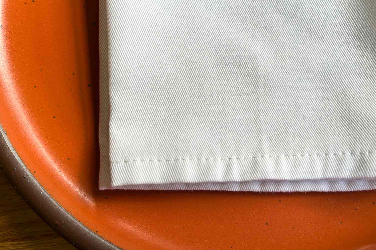 A close-up of a white napkin on the edge of an orange plate