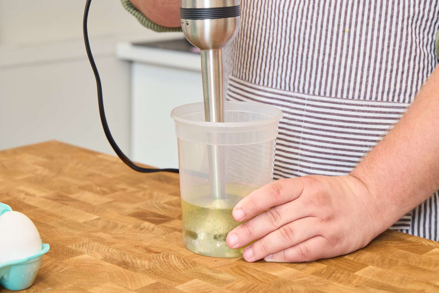 A person uses the All-Clad Stainless Steel Immersion Blender in a plastic container