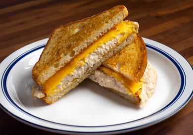 A tuna melt sandwich on a plate, cut in half diagonally to make triangles; showing melted yellow American cheese slices on top of a creamy tuna salad and nicely toasted bread.