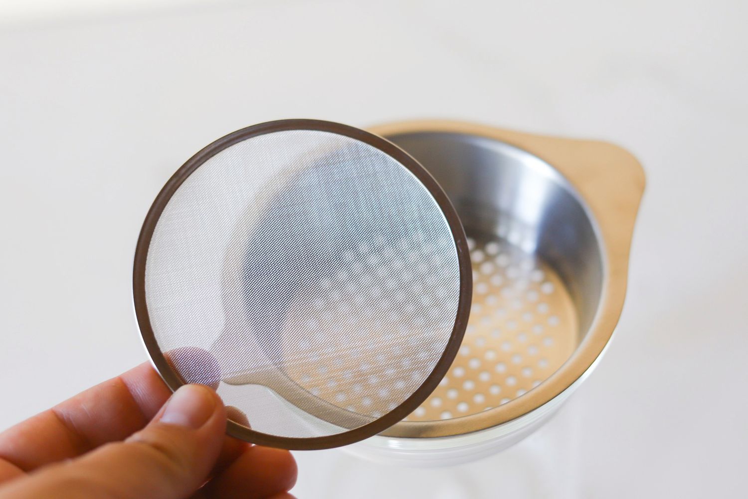 A person holding a fine mesh sieve over a fat separator