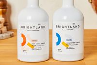 Two bottles of Brightland extra virgin olive oil labeled Awake and Alive on a wooden surface