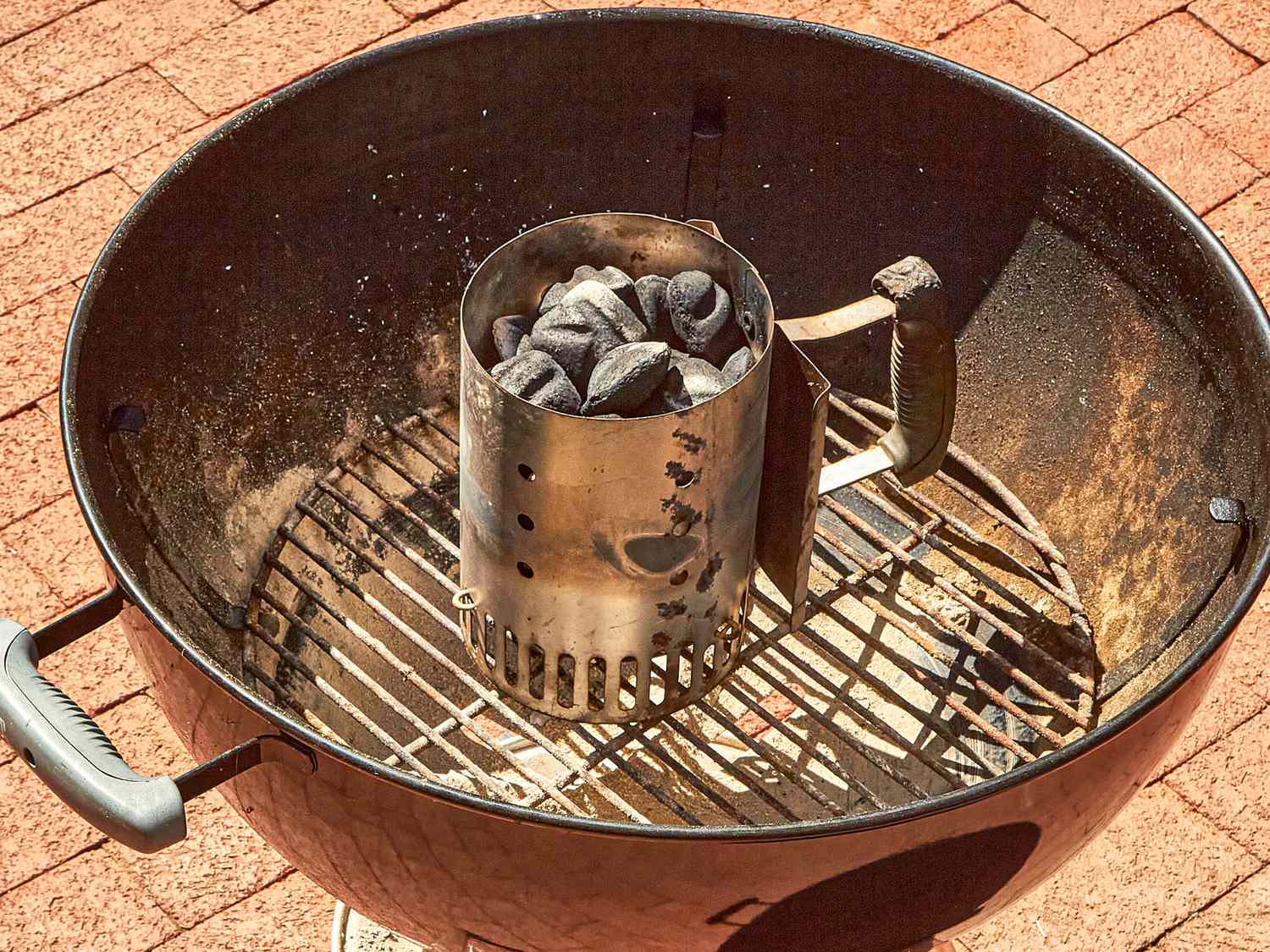 A charcoal chimney starter inside a grill with charcoal bricks in it preparing for cooking on a barbecue