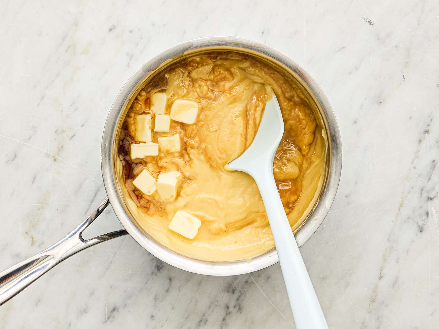 Butter and caramel sauce being mixed in a saucepan with a white spatula