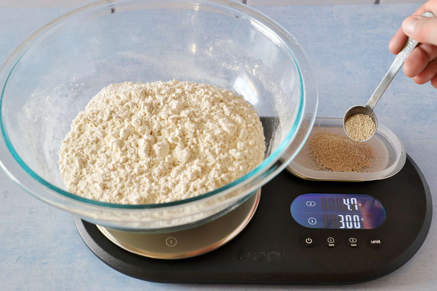 A person using a dual platform kitchen scale to weigh flour and yeast at the same time