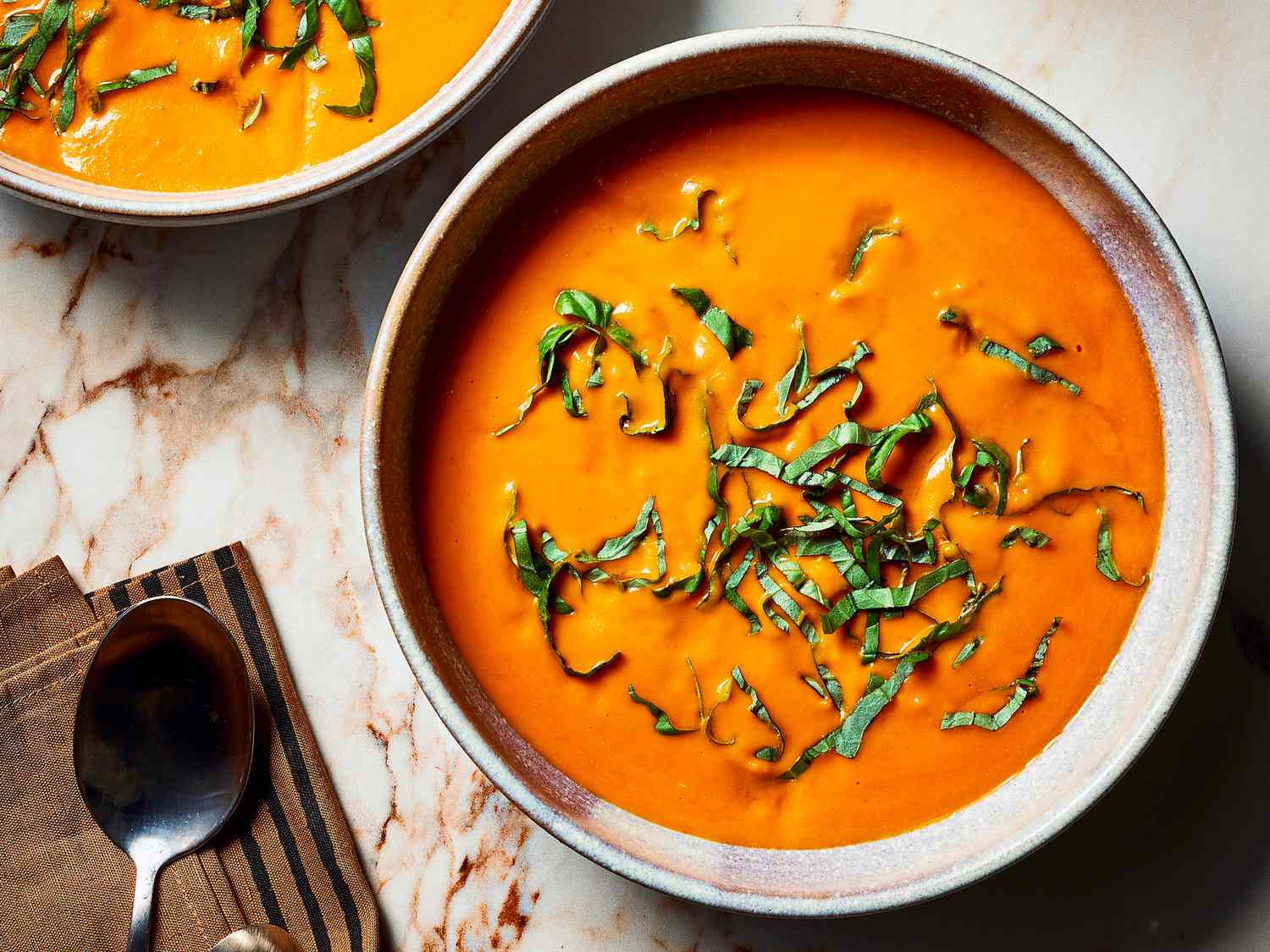 Overhead view of two bowls of tomato soup with shredded greens on top