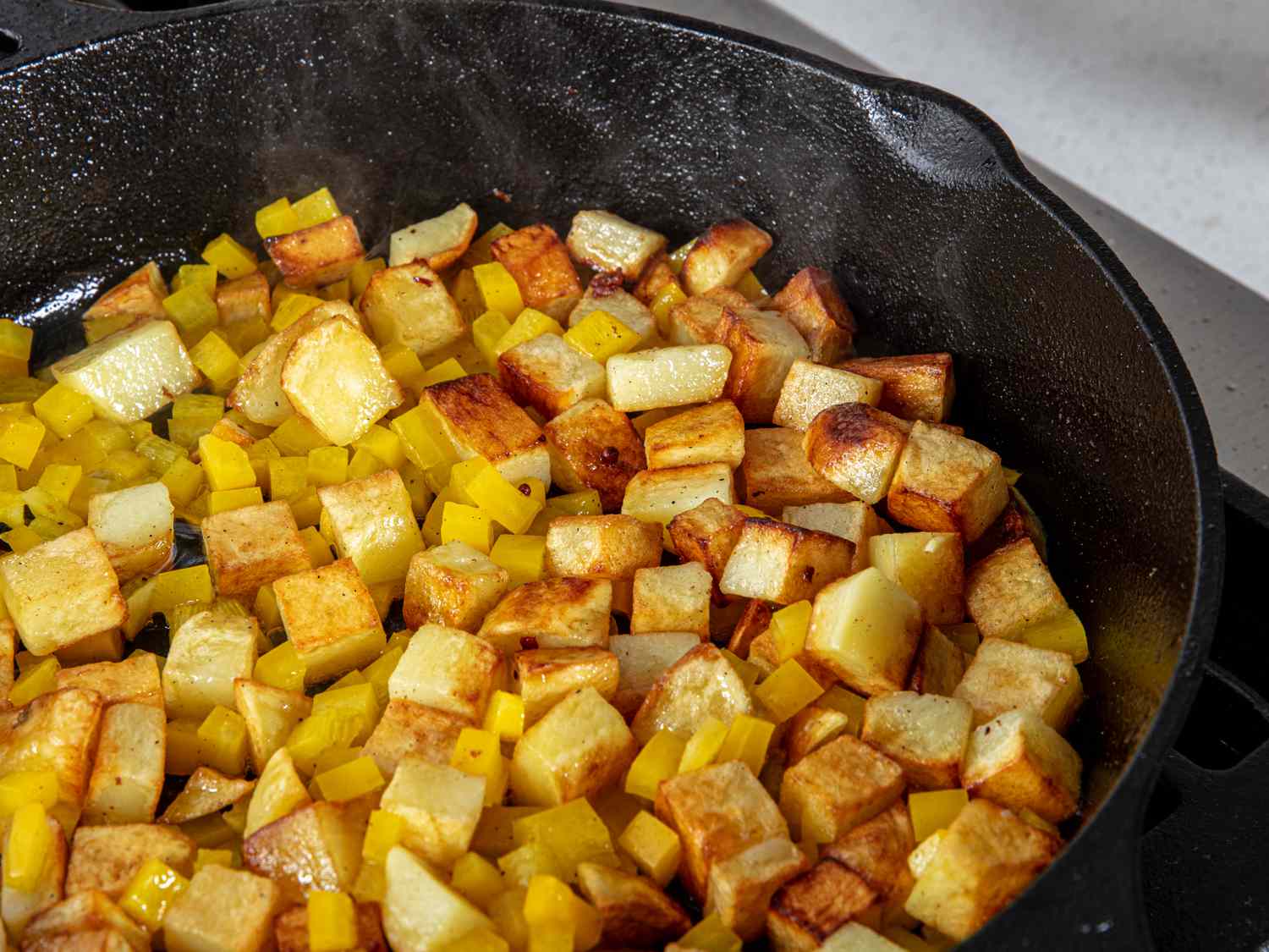 Cubes of browned potato cubes and diced yellow pepper in a cast iron skillet
