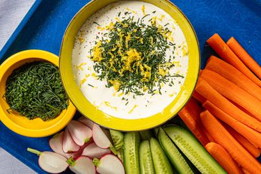 Whipped cottage cheese topped with fresh herbs and lemon zest next to raw vegetables.