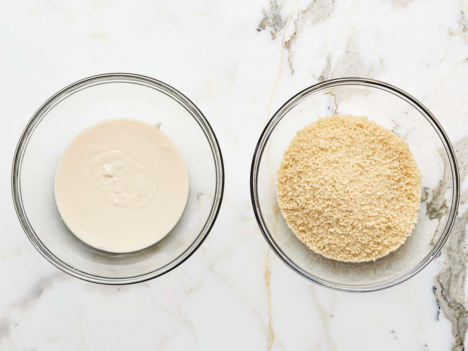 Overhead view of two bowls with flour-water mixture and breadcrumbs