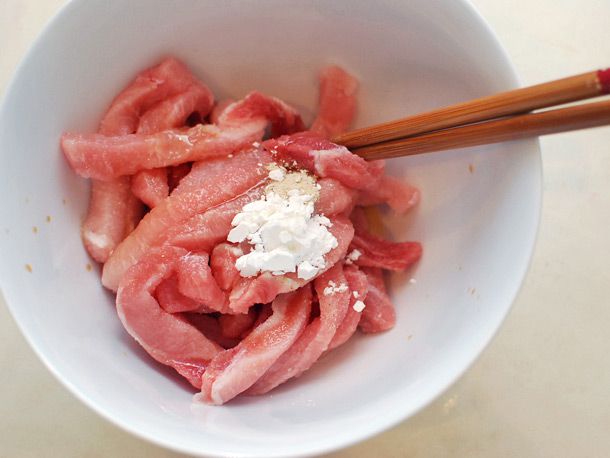 Raw pork loin strips mixed with cornstarch and seasonings with chopsticks