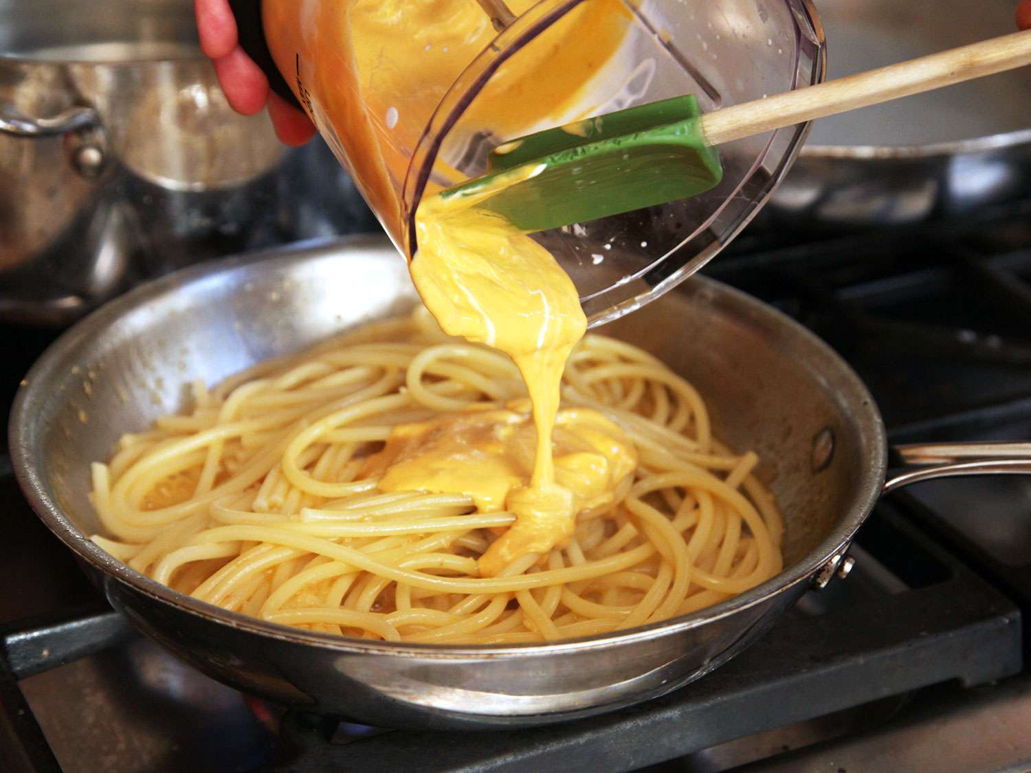 Using a rubber spatula to scrape sea urchin/crema purée from a blender jar into a skillet of spaghetti.
