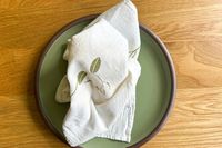 A folded cloth napkin with a leaf design on a green plate